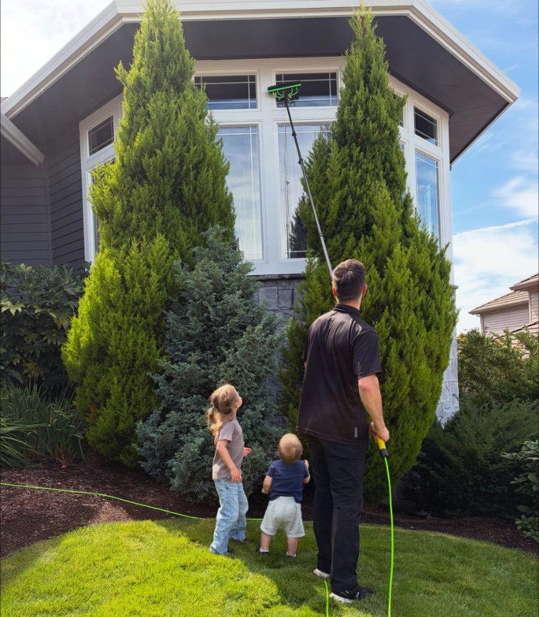 Elijah cleaning second-story windows with a water-fed pole while his two young children watch
